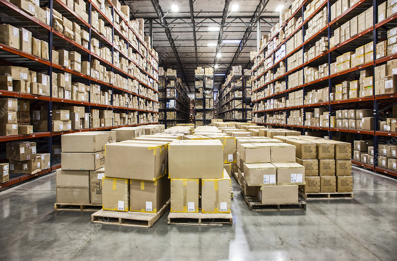 View down aisles of racks holding cardboard boxes of product on pallets in a large distribution warehouse